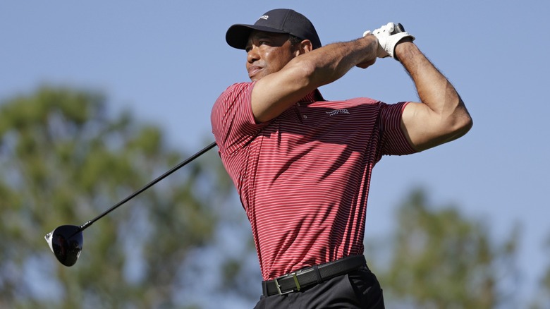 Tiger Woods swinging a golf club wearing a red and white striped shirt and a black baseball cap