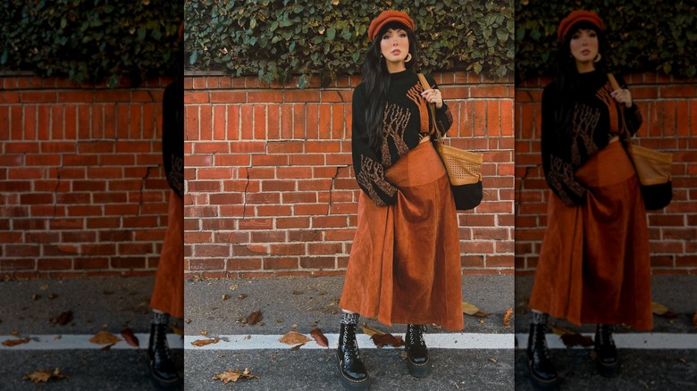 A woman in a burnt orange maxi skirt with low boots outside