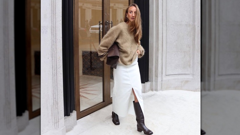 A woman with a white skirt with a front slit and brown boots walking outside