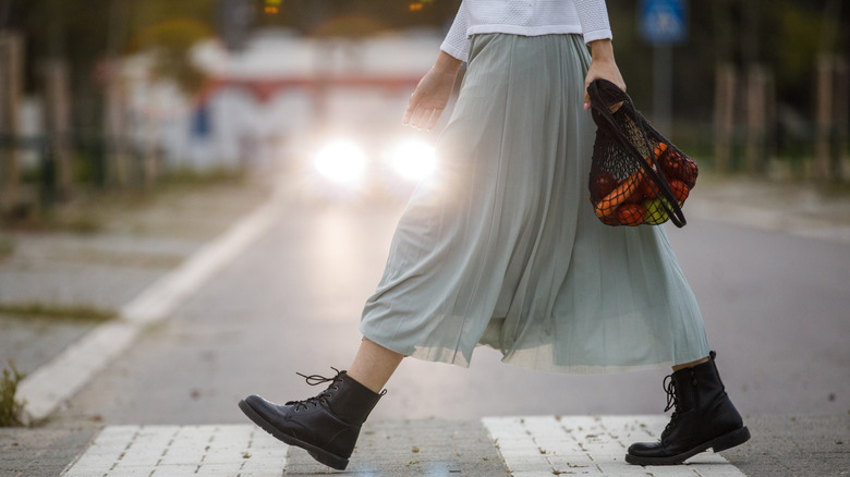 Woman wearing skirt and combat boots holding produce in netted bag