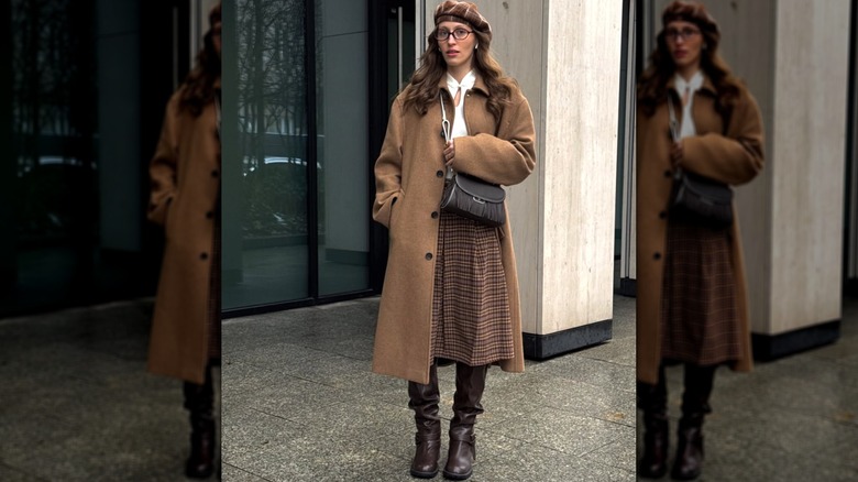 A woman wearing a beret and brown coat with a skirt and boots outside