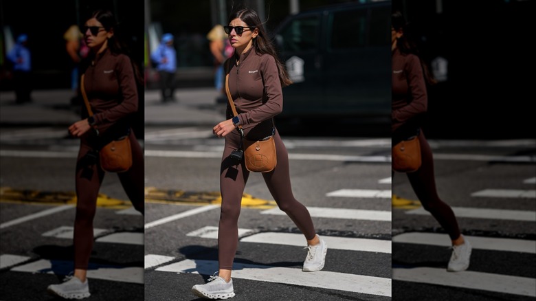 A woman in brown leggings and white sneakers crossing the street