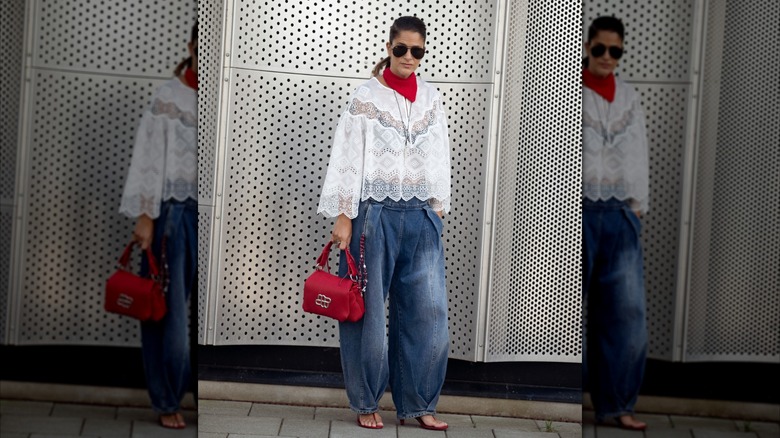 A woman wearing barrel-leg jeans and a lacy white top with a red purse