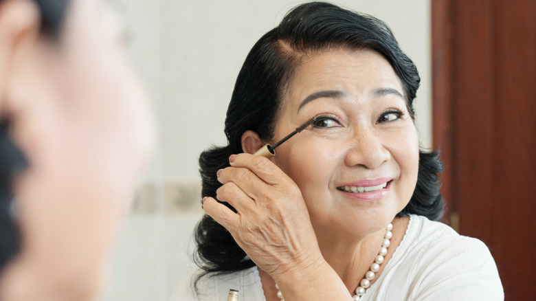 Older woman smiling while applying mascara in the mirror