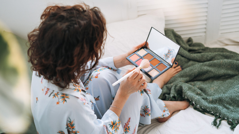 Over the shoulder snapshot of brunette woman in pajamas holding as face-sculpting palette