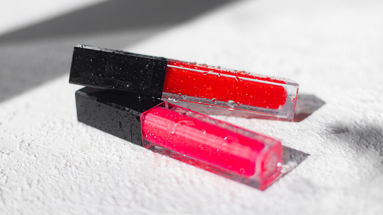 Two tubes of bright lip colored stacked and splattered with water drops in speckled sunshine