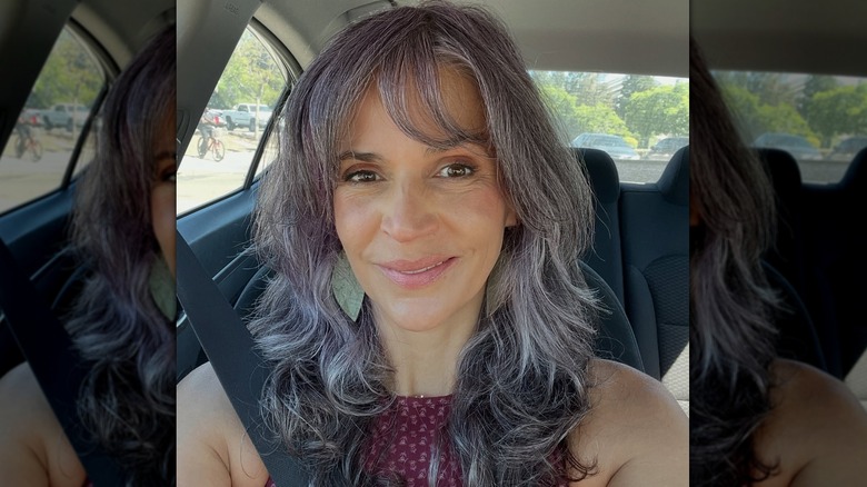 A woman posing in a car with a short, gray and purple shag haircut