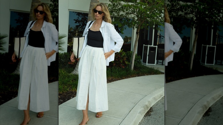 A woman wearing a black swimsuit as a bodysuit under an open white shirt and a white skirt