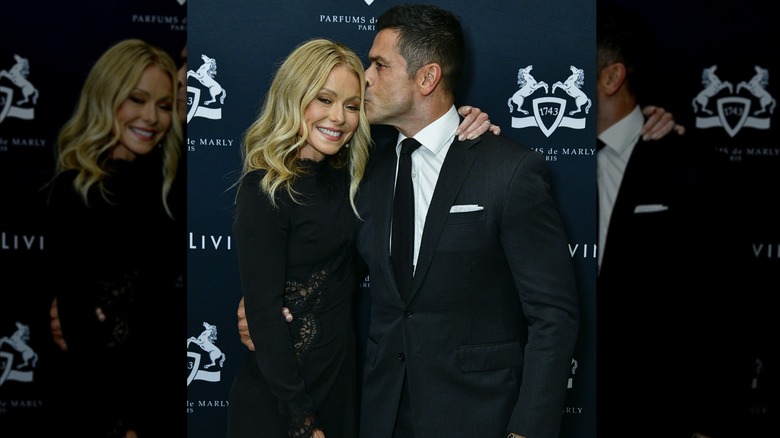 Kelly Ripa smiling and Mark Consuelos giving her a kiss on the temple