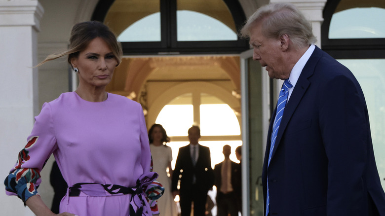 Melania Trump in a purple dress standing with Donald Trump in a blue suit