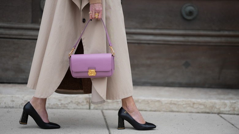 A woman walking in the street wearing tan, black pumps, and a purple puse