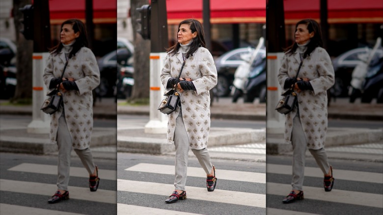 An older woman walking in the street wearing mostly neutrals