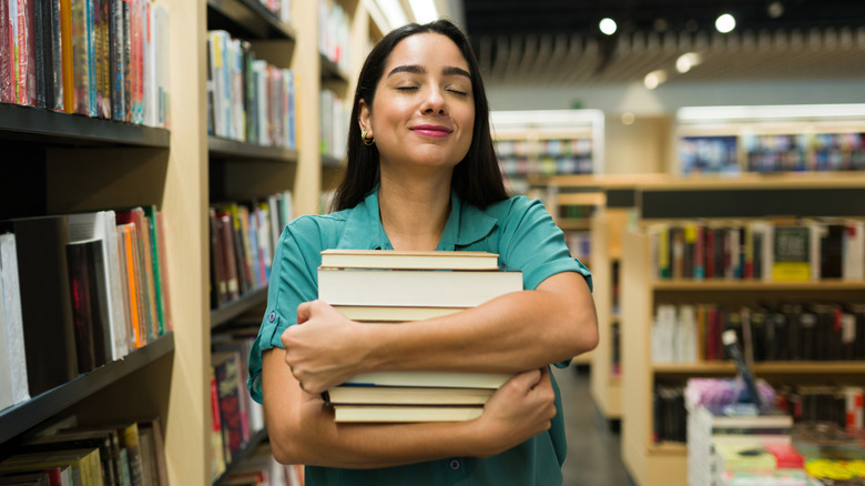 Dark-haired woman hugging a stack of books while standing in a bookstore