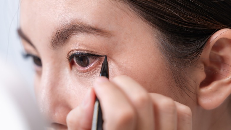 A woman applying black eyeliner to her upper eyelid