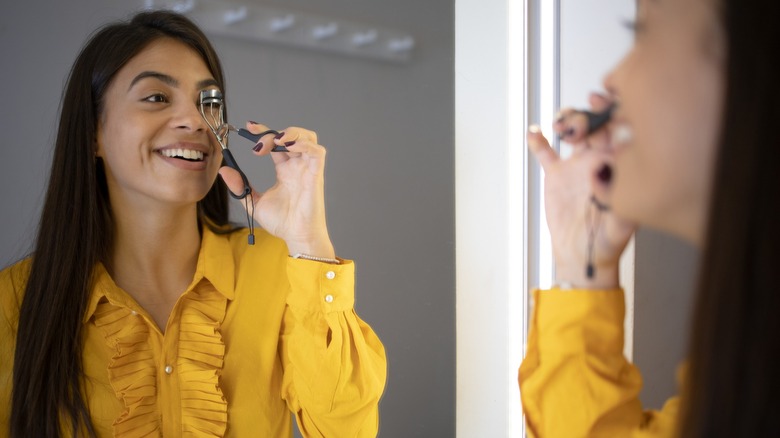 A woman smiling in the mirror while curling her eyelashes