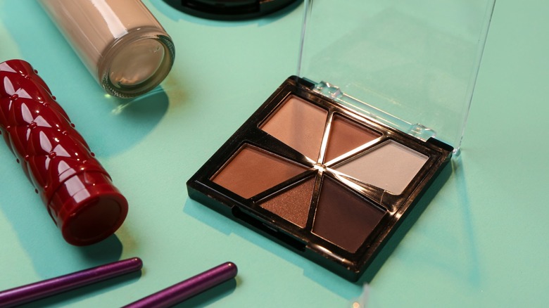 An eyeshadow palette with natural colors next to other makeup