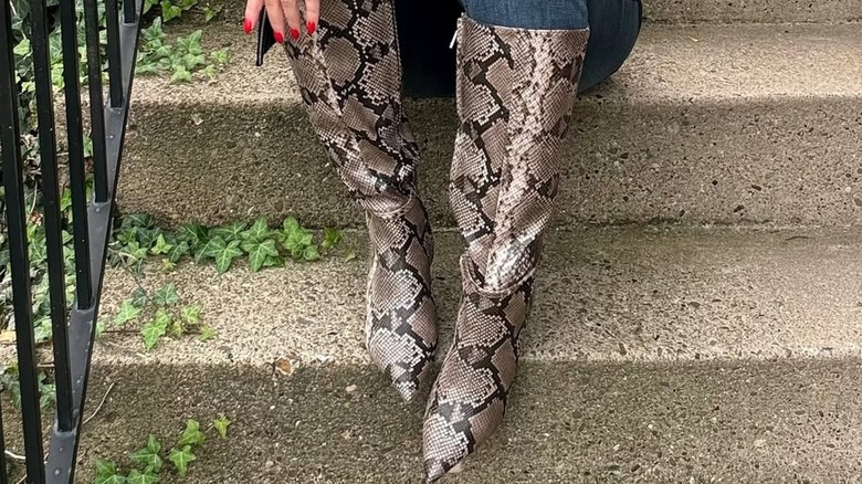 A woman sitting down in snakeskin boots
