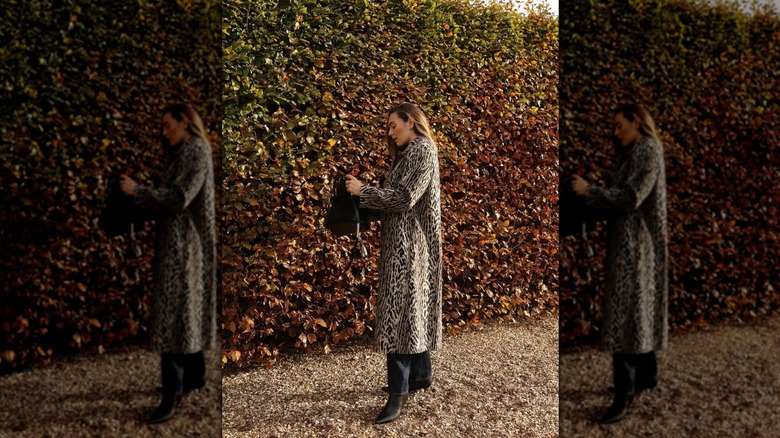A woman standing in front of a hedge and wearing a full-length animal print coat