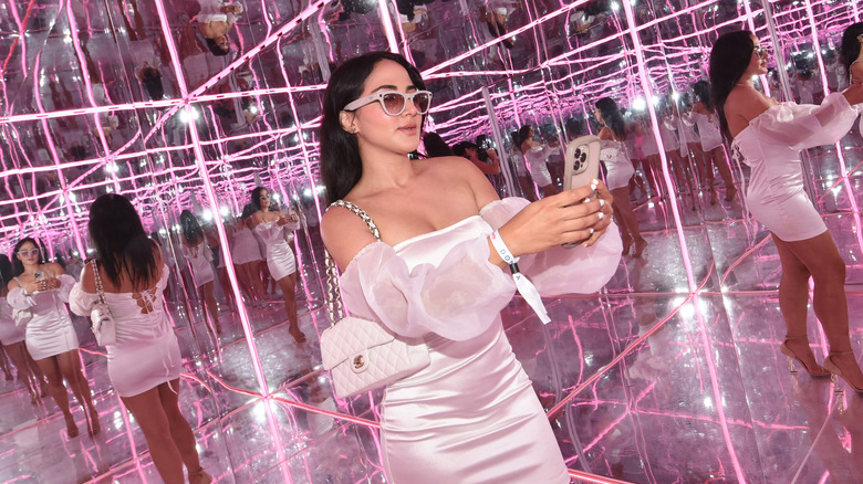 A woman takes a selfie inside a red mirror room while wearing a white dress