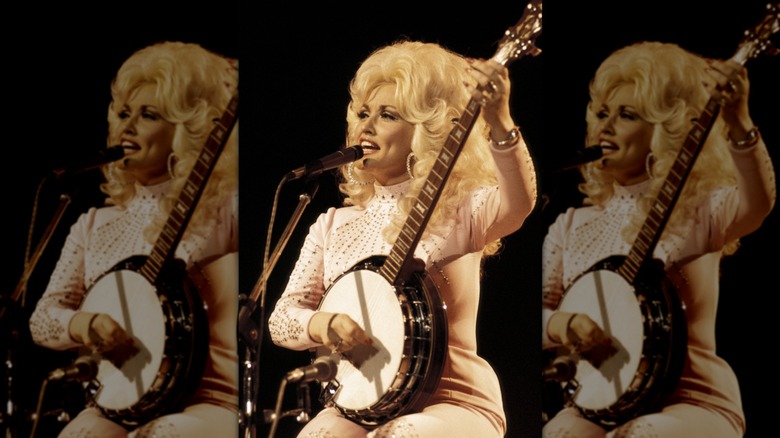 Dolly Parton playing banjo on stage in a pale pink matching suit