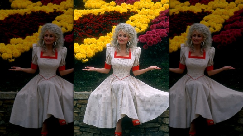 Dolly Parton sitting on a wall in a white and red dress