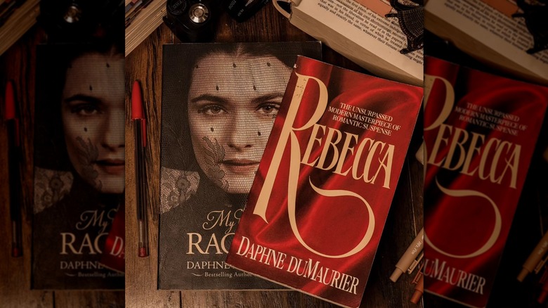Top down view of two copies of "Rebecca" by Daphne DuMaurier, surronded by slightly-visible books and a red pen