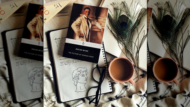A top-down view of a copy of "The Picture of Dorian Gray" over multiple open journals and next to glasses and a mug