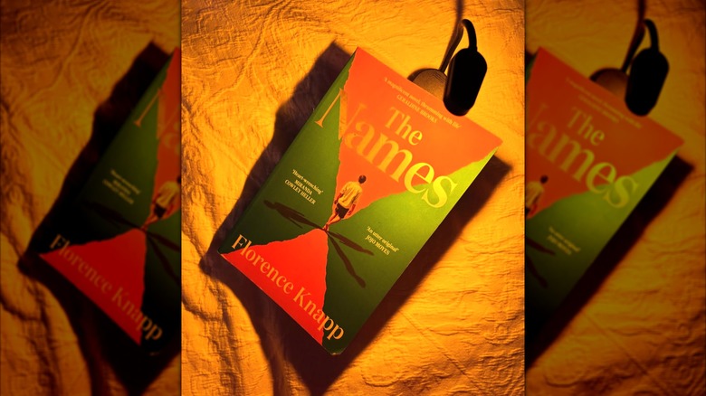 A portable book light clipped into a book over an orange blanket