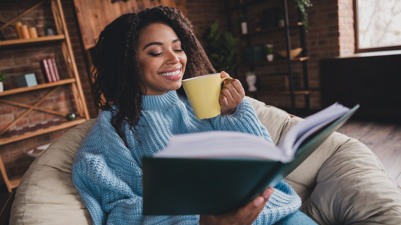 A woman reading a book wearing a thick blue sweater