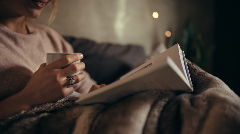 A woman sitting on a couch with a cup of tea and reading a book