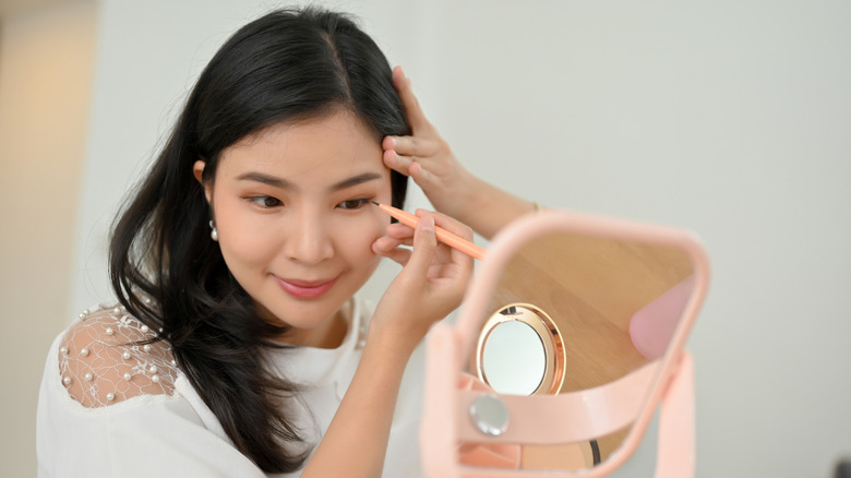 Woman applying eyeliner while looking in mirror