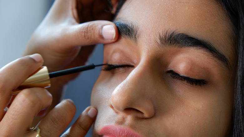 Woman with eyes closed getting eyeliner applied for her