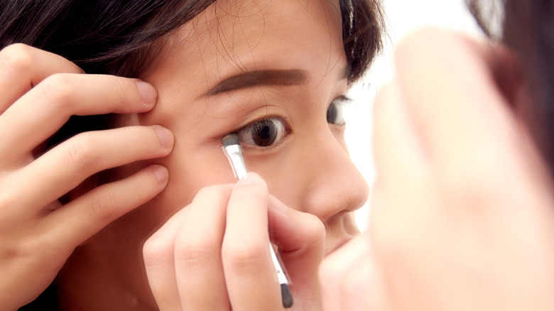Woman applying eyeliner with brush while tugging her eyes