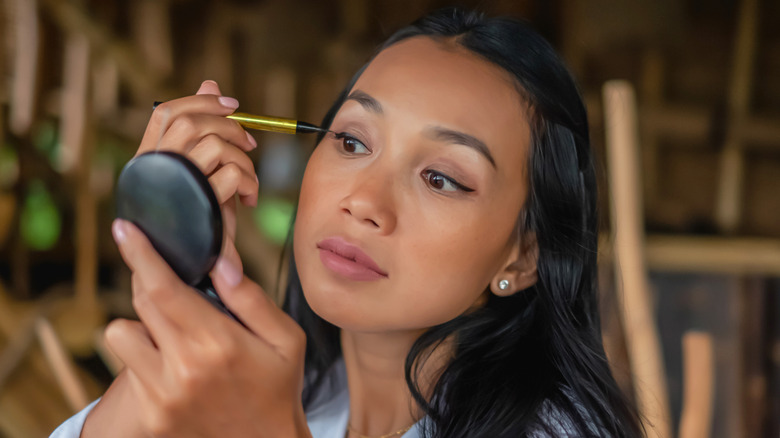 Woman applying eyeliner while looking in small compact mirror