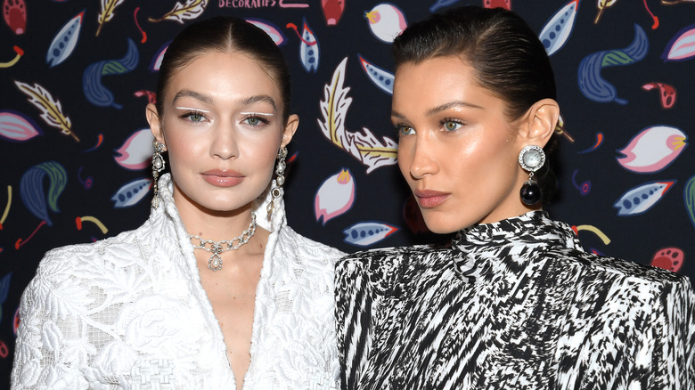 Gigi and Bella Hadid standing together at a Harper's Bazzar event, each wearing structured dresses