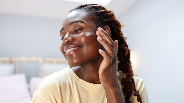 A woman applying lotion to her face smiling
