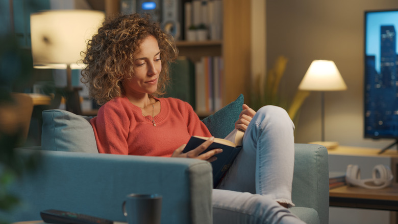 A person reading a book and sitting in a chair with a lamp over their shoulder
