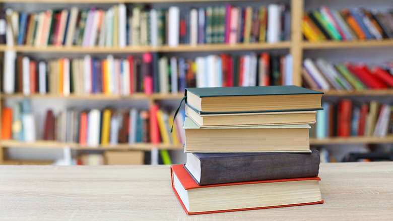 A stack of books on a table with full bookshelves in the background