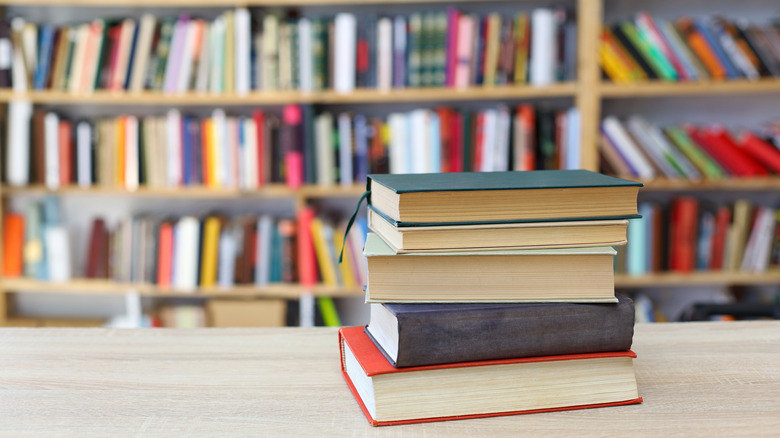 A stack of books on a table in front of several bookshelves