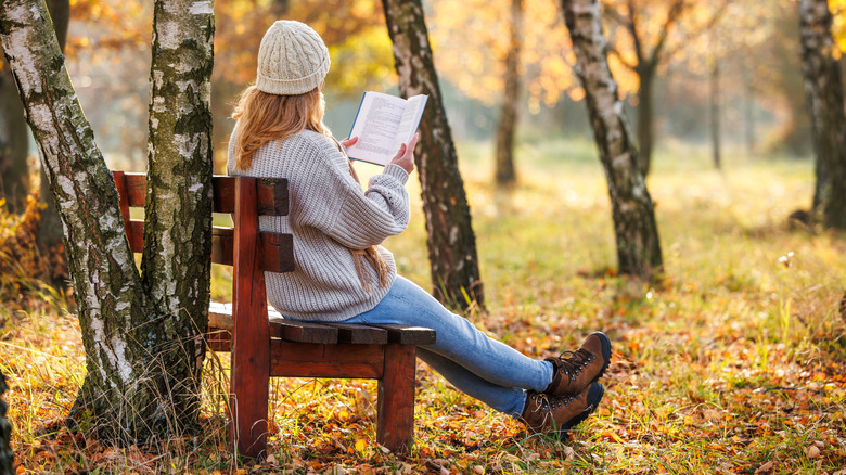 A woman reading on a bench surrounded by trees