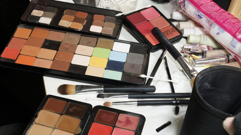 Various makeup brushes laid flat with three makeup colour cosmetic palettes