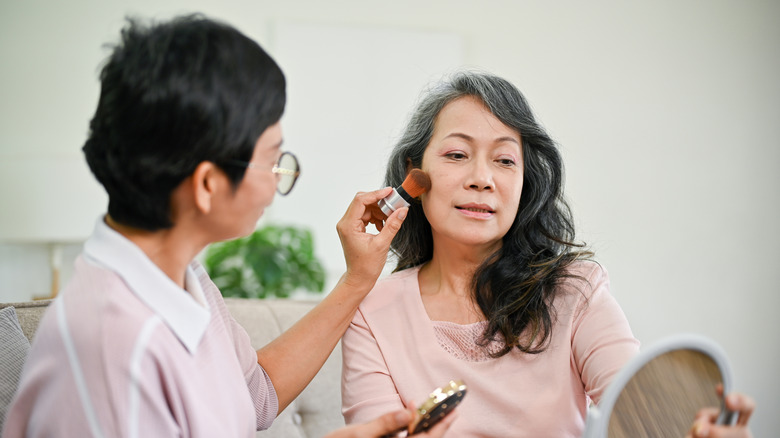 Women applying makeup to friend in pink longsleeve top