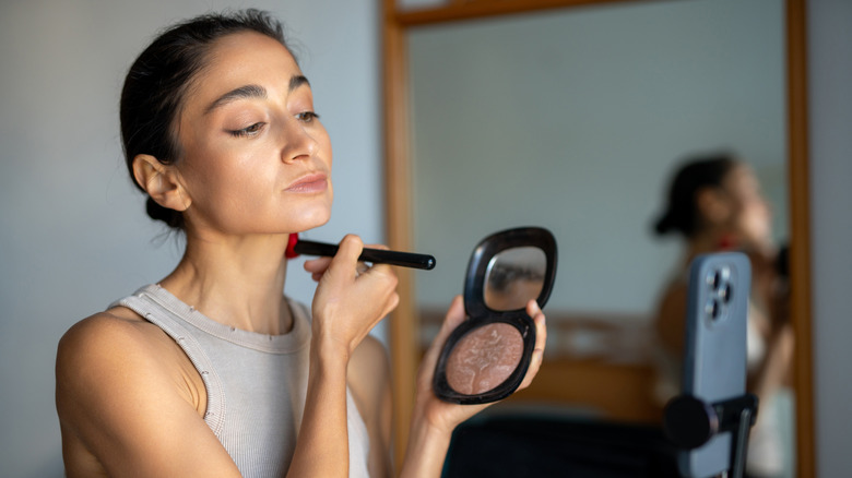 Women applying bronzer to her neck whilst looking at her phone camera
