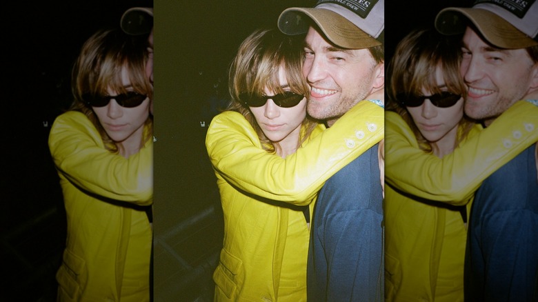 Suki Waterhouse embracing Robert Pattinson while he smiles and looks to the side