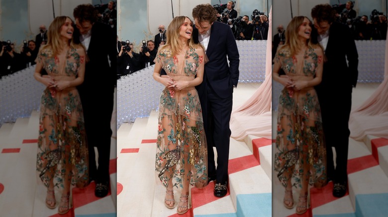 Suki Waterhouse laughing into Robert Pattinson's face as he leans his head down and holds her waist at the 2023 Met Gala