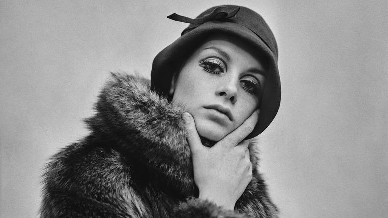 Twiggy posing in a fur coat and cloche hat while wearing her signature eye makeup