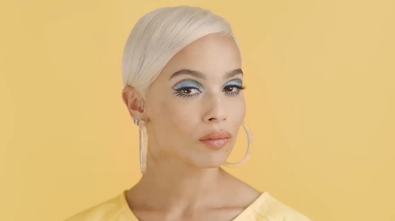 Zoë Kravitz posing against a yellow background while wearing bold eyeliner and blue eyeshadow