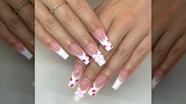 Two overlapping hands showing a coquette-style nail design featuring hand-drawn strawberries and 3D bows
