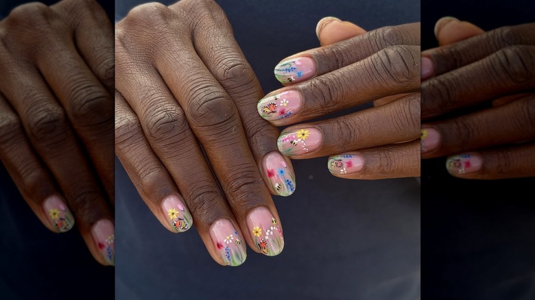 Two angled hands showing a garden nail design decorated with butterflies and bees
