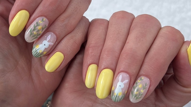 Two folded hands showing nude nails with flowers and bunnies alongside yellow accent nails